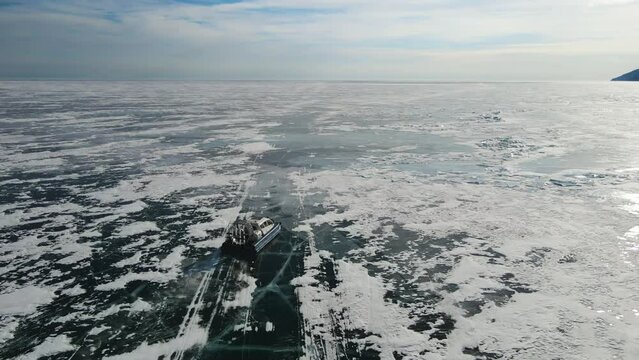 A slow-motion aerial shot. Passenger transportation on Lake Baikal. Hovercraft (amphibious capable of travelling over water and ice) drifting over smooth ice. Snow flying out from under air cushion.