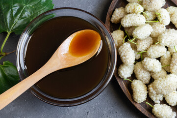 White mulberry molasses in glass bowl and wooden spoon with fresh mulberries, healthy food