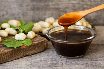 White mulberry molasses in glass bowl and wooden spoon with fresh mulberries, healthy food