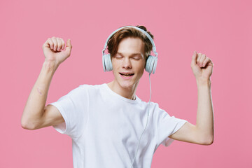 happy young man in a white t-shirt emotionally and joyfully listens to music in bright headphones raising his hands up