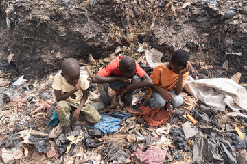 Three little African boys sitting on a landfill suffering from breathing problems, burning eyes,...