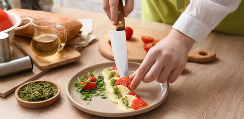 Woman preparing caprese salad with pesto sauce in kitchen
