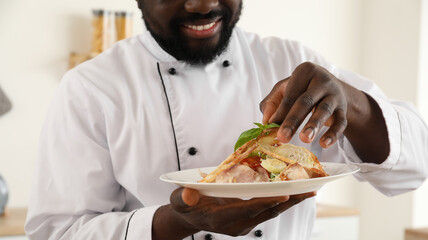 Male African-American chef with tasty caesar salad in kitchen - obrazy, fototapety, plakaty