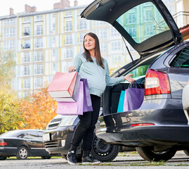 Woman with belly puting shopping bags in vehicle trunk, enjoying maternity and parenthood in awaiting mode. Pregnant female with purchase preparing for baby birth during weekend in city.