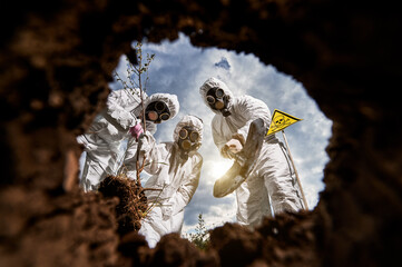 Concept of post apocalypse - people in white overalls and gas masks reforesting DEATH ZONE after hazard radioactive catastrophe on earth. Ecologists planting seedling. View from earth pit.