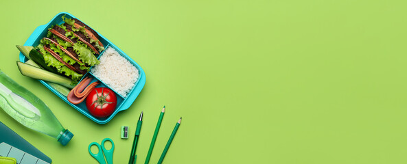 Lunch box with tasty food, bottle of water and school stationery on green background with space for...