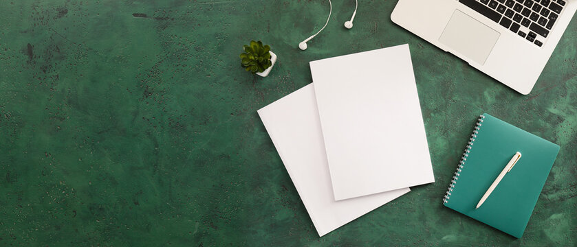Blank magazines, laptop and notebook on green background with space for text