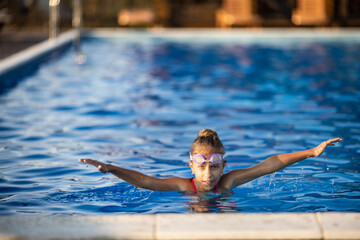A girl in a bright swimsuit with swimming goggles dives into a pool with clear transparent water