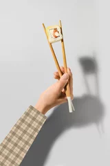  Woman holding wooden chopsticks with delicious sushi roll on light background © Pixel-Shot