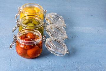 Homemade Pickles Canned Food Cucumbers Cherry Tomatoes and Small Yellow Squash on Blue Background Copy Space