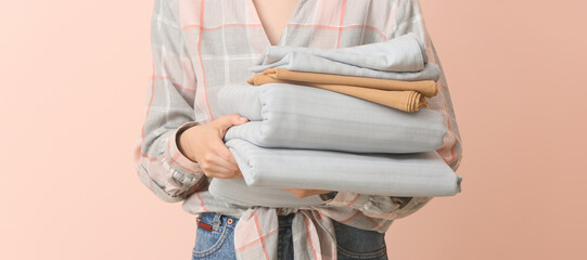 Woman holding stack of clean bed sheets on color background