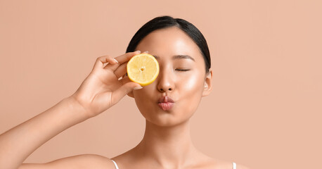 Fototapeta na wymiar Pretty young Asian woman with lemon on beige background
