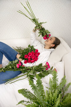  A young, beautiful girl lies on the bed and happily smells roses. Flowers are scattered on the bed. The concept of romance, holiday, birthday, anniversary, March 8, valentine's day High quality photo