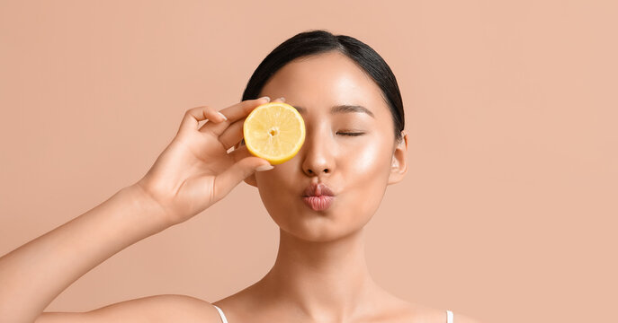 Pretty young Asian woman with lemon on beige background