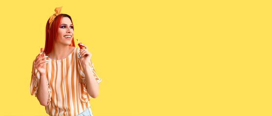 Stylish transgender woman applying lipstick against yellow background with space for text