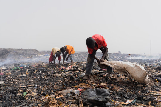 Three small African children searching for recyclable valuables at the garbage dump amidst piles of waste, dirt and smoldering smoke