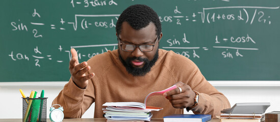 Displeased African-American teacher checking homework in classroom