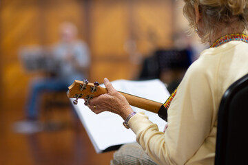 detail of senior lady playing ukulele with blurred musician in background