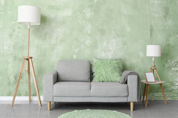 Comfortable grey sofa with lamps and table near green wall in living room