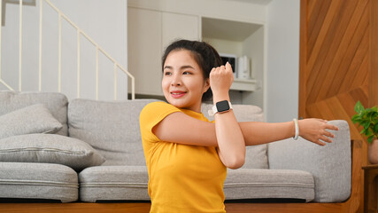 Charming asian woman doing stretching arm, warming up before workout at home