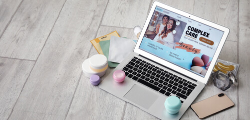 Laptop with open page of beauty blog, mobile phone and cosmetic products on light wooden floor with...