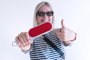 A happy woman holds a red electrostatic clothing brush and shows thumbs up on a white background....