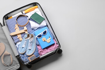 Opened suitcase with different accessories for travelling on grey background