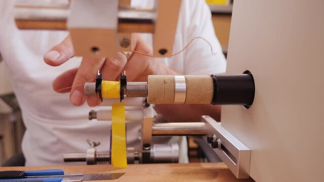 Hand making electronic component using coil winding machine - reeling conducting wire on plastic support to manufacture a transformer part, close up, camera slide