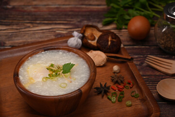 Rice porridge with boiled egg ,sliced ginger and slice scallion on wooden table. Congee is a type of rice porridge popular in many Asian countries