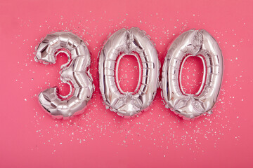 From above of silver shiny balloons demonstrating number 300 three hundred pink background with scattered glitter - obrazy, fototapety, plakaty