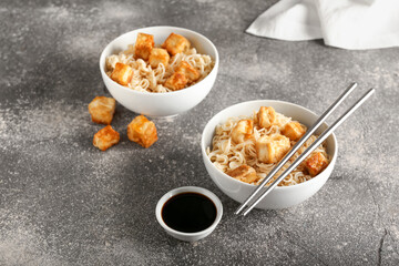 Bowls of tasty noodles with chicken and sauce on grey background