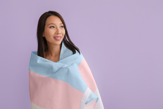 Young Asian woman with transgender flag on lilac background
