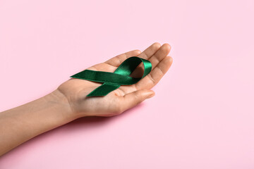 Hand with green ribbon on pink background. Liver cancer concept