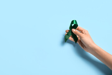 Hand with green ribbon on light blue background. Liver cancer concept
