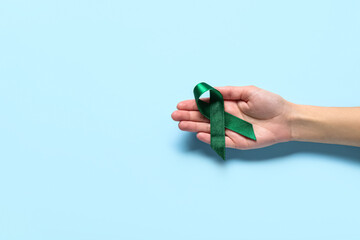 Hand with green ribbon on light blue background. Liver cancer concept