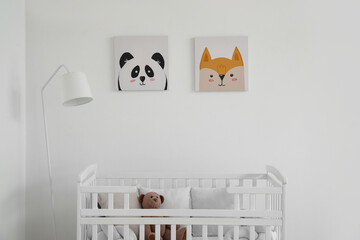 Interior of light nursery with baby crib, lamp and pictures