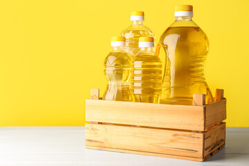 Bottles of sunflower oil in wooden box on table against yellow background