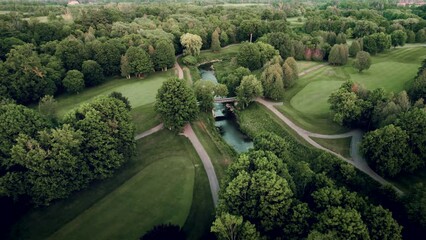 Aerial view of lush scenic golf course with river and bridge drone fly over at sunset in summertime