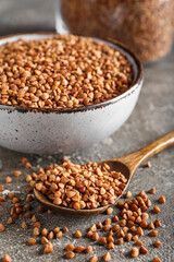 Wooden spoon and bowl with buckwheat grains on grunge table, closeup