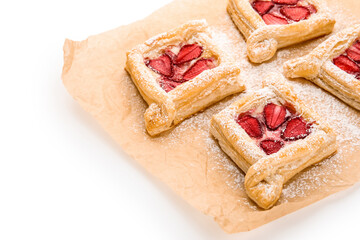 Parchment paper with strawberry puff pastries and sugar powder on white background