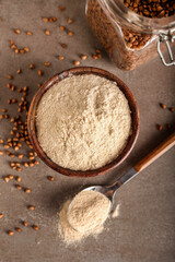 Bowl of flour and spoon with buckwheat grains on grunge background