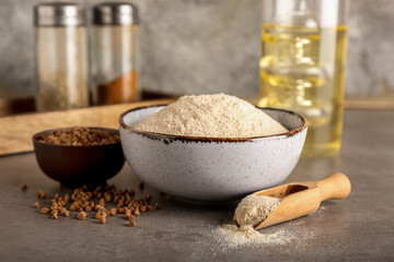 Bowls with flour, buckwheat grains and scoop on table