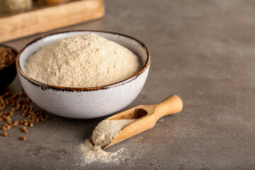 Bowl of flour, scoop and buckwheat grains on grunge background