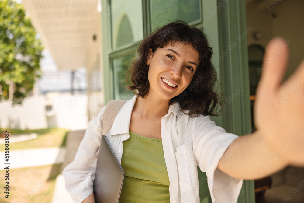 Wall mural Beautiful young caucasian woman smiling looking at camera taking selfie outdoors. Brunette with bob haircut wears t-shirt with shirt. Lifestyle concept