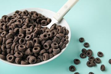 Bowl with black cereal rings on blue background, closeup