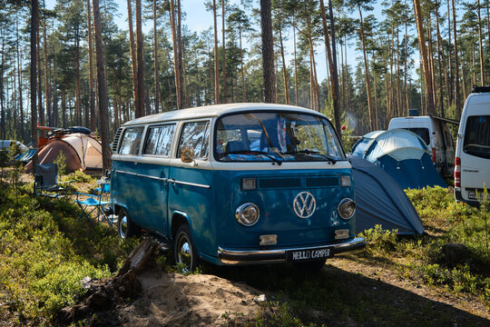 Leningrad Region, Russia - June 2022. Festival mobile homes in coniferous forest. Camping for tents and cars. Mobile home based on retro Volkswagen Transporter minivan blue chrome wheels and mirrors.