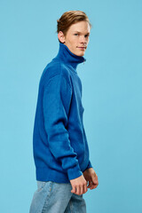 a handsome young man in an autumn blue sweater stands on a light background with an empty space for...