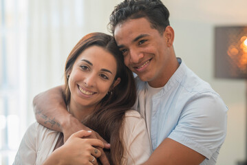 Concept of young interracial couple in love and relationship. Boy hug and protect girlfriend at home. Life and future together man and woman. New apartment happiness satisfaction portrait. Smile