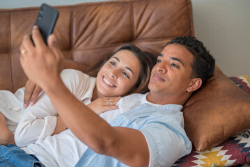 Young couple in love enjoy and use modern mobile phone together laying and relaxing on the sofa. Love and relationship young people indoor leisure activity with internet connection. Video call concept