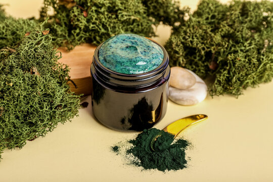 Jar of spirulina facial mask and powder on color background